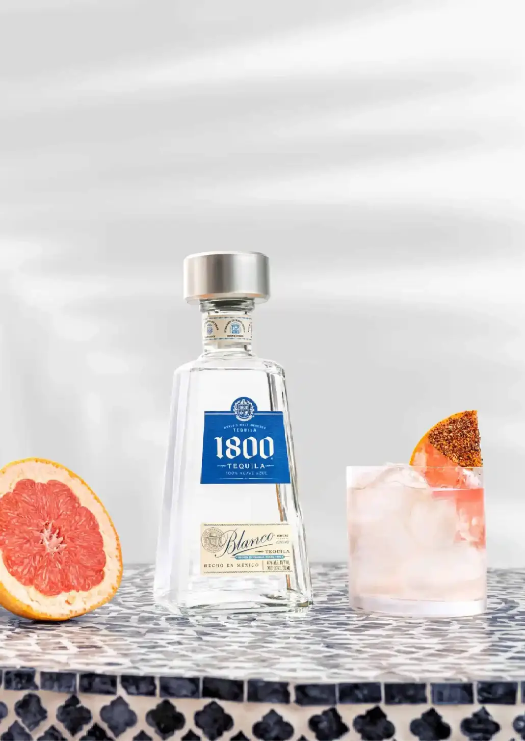 bottle of 1800 tequila, half a grapefruit and paloma cocktail on a table